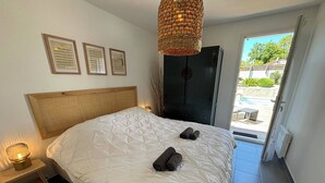 Un dormitorio con una cama grande, una mesita de noche con lámpara, una puerta que da a un balcón y diplomas enmarcados en la pared.