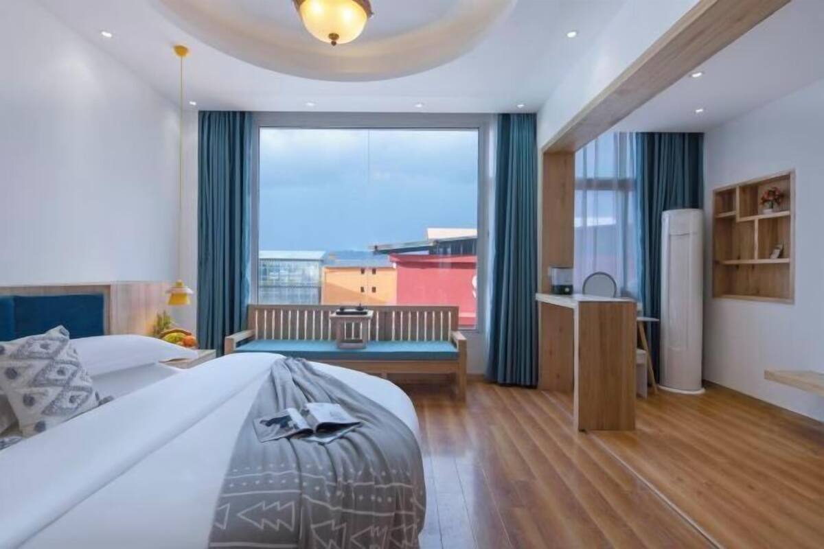 Une chambre d’hôtel moderne, dotée d’un grand lit, d’une banquette près de la fenêtre, d’un bureau et offrant une vue sur le paysage urbain.