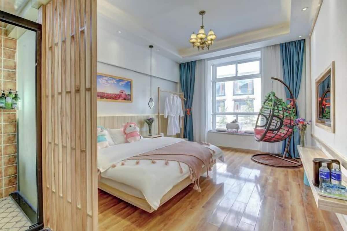 Une chambre à coucher avec un lit, un fauteuil suspendu, une fenêtre avec des rideaux, une étagère fixée au mur et un tableau.