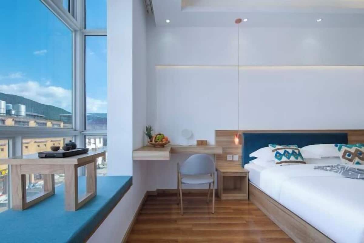 Une chambre d’hôtel moderne dotée d’une grande fenêtre, d’un bureau, d’une chaise, d’un lit avec des oreillers et d’une table de chevet.