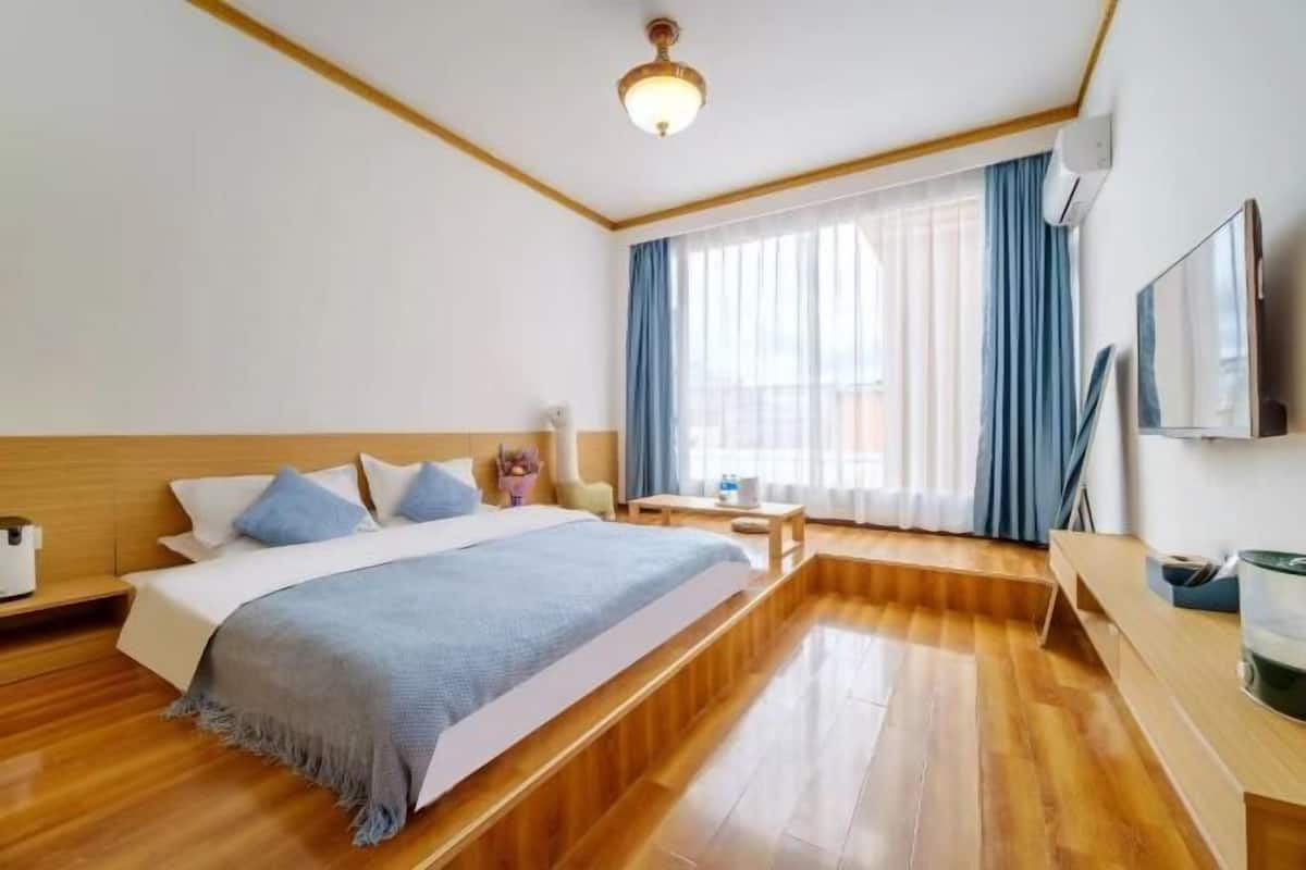 Une chambre d’hôtel avec un plancher en bois, un lit recouvert d’une couverture bleue, un téléviseur fixé au mur et une fenêtre avec des rideaux bleus.