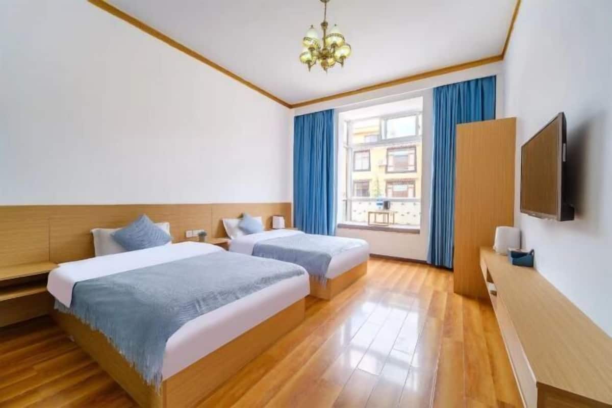 Une chambre d’hôtel avec deux lits, un plancher en bois, une télévision et une fenêtre avec des rideaux.