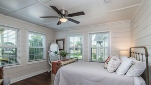 Un dormitorio con cama, ventilador de techo y amplias ventanas.