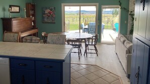 A dining area with a table and chairs, a bench, a cabinet, and a view of a vineyard through a glass door. - Vineyard views at Dichotomy Vineyards guest house in the Yakima Valley (Outlook)