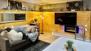 Un salon chaleureux avec un grand téléviseur à écran plat, un canapé confortable, une cheminée et des boiseries.