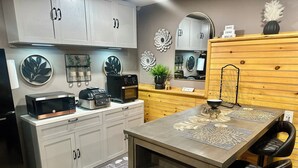 Une cuisine moderne avec des meubles gris, un four à micro-ondes, une machine à café et une table à manger en bois avec un set de table.