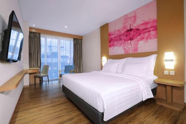 A hotel room with a large bed, a TV mounted on the wall, a chair, a desk, and a large window with curtains. - Favehotel Nagoya - Batam (Nagoya)