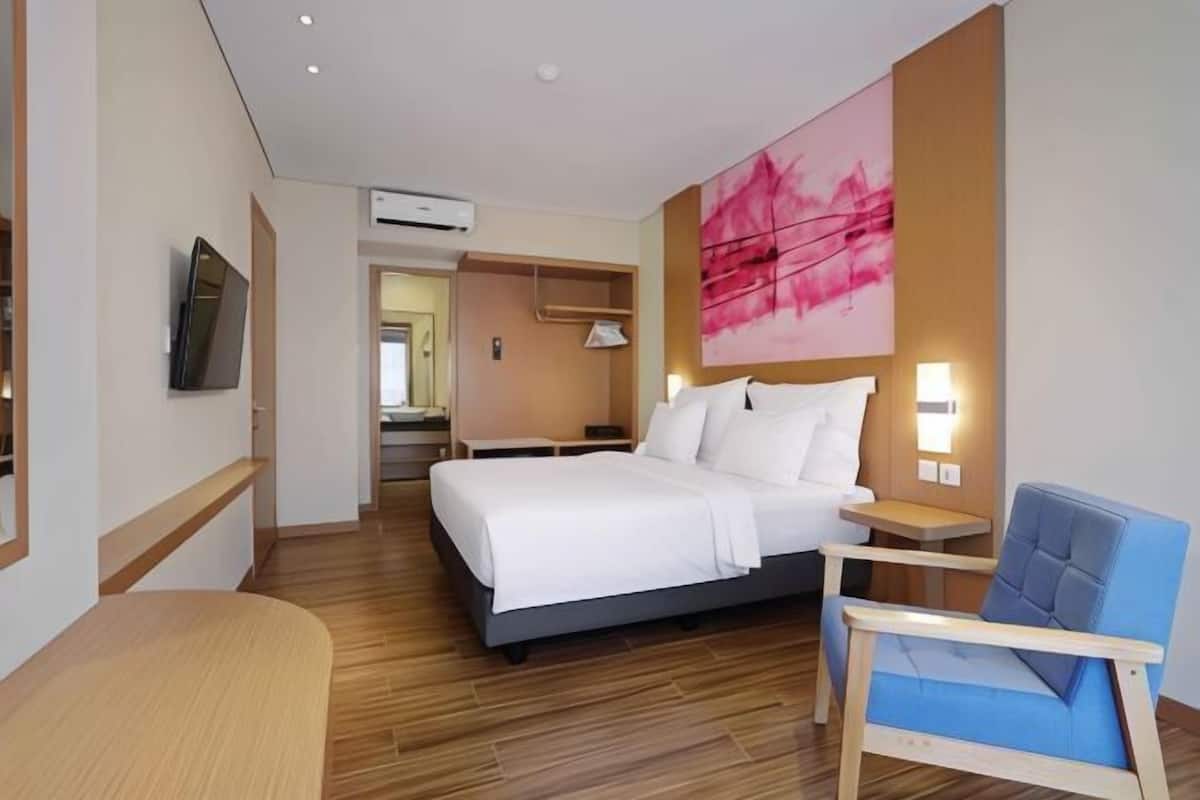 A hotel room with a bed, a chair, a TV, and a painting on the wall.