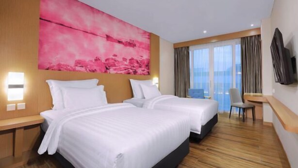 A hotel room with two beds, a large pink artwork on the wall, a TV mounted on the wall, and a view of the outside through the window. - Favehotel Nagoya - Batam (Nagoya)