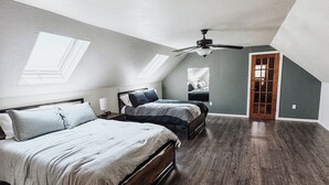 Une chambre avec un plafond en pente, des fenêtres de toit, un ventilateur de plafond, un lit, un banc et une porte.