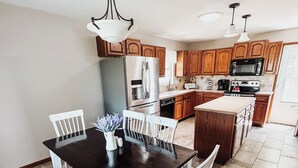 Une cuisine moderne avec des meubles en bois, un îlot central et un coin repas comprenant une table sombre et des chaises blanches.