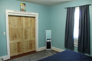 A bedroom with a wooden wardrobe, a bed, a mirror, and a window with curtains.
