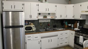 Una cocina con armarios blancos, un refrigerador de acero inoxidable, un microondas, un fregadero y una estufa.