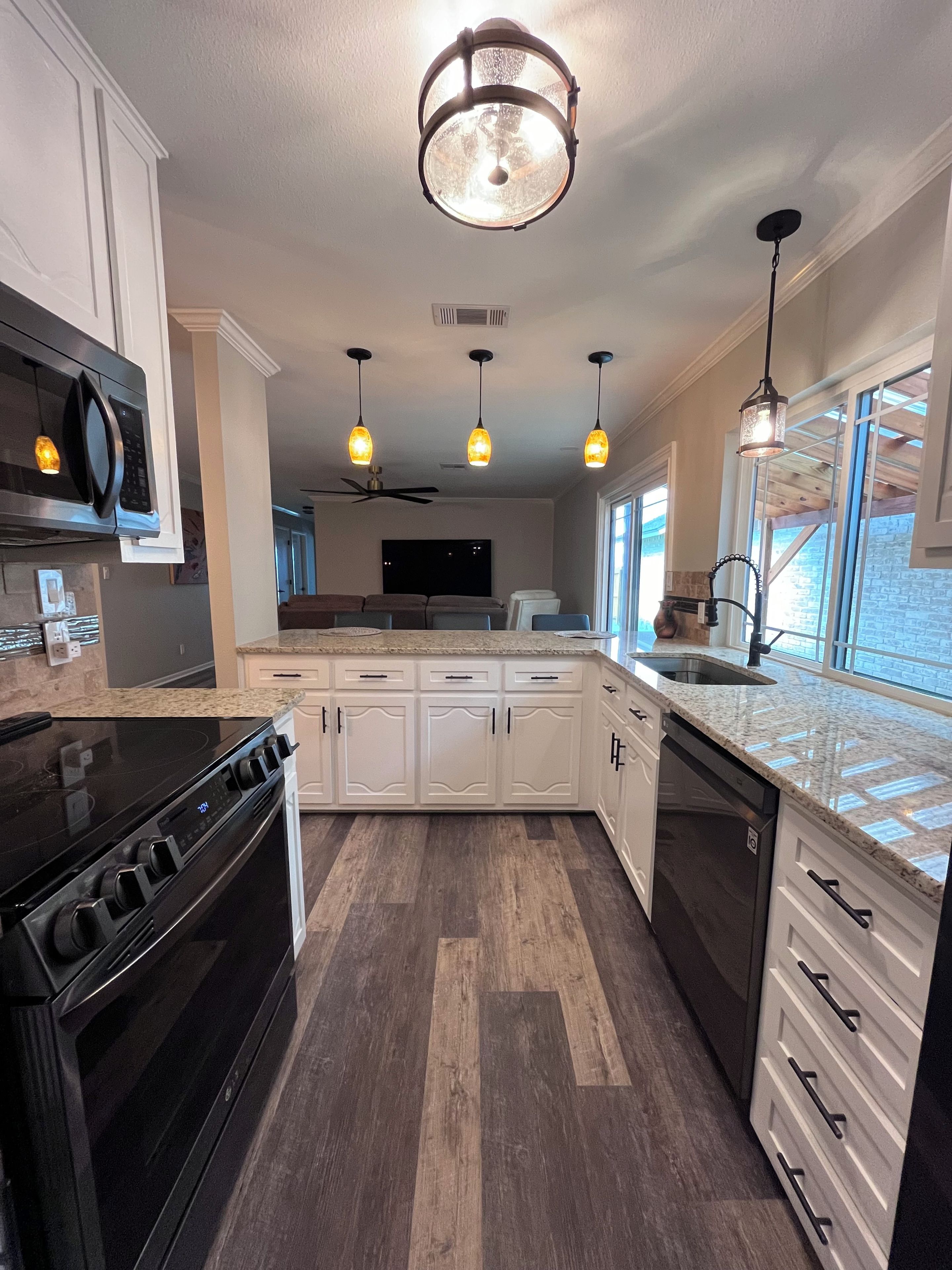 A modern kitchen with a central island, built-in appliances, pendant lighting, and a view to the outside.
