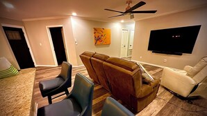 A living room with a TV, leather sofas, and a dining area with chairs.