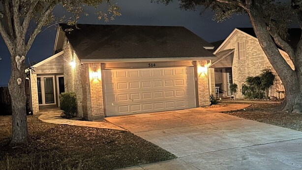 A residential house with a garage, a driveway, and a large tree in the foreground.