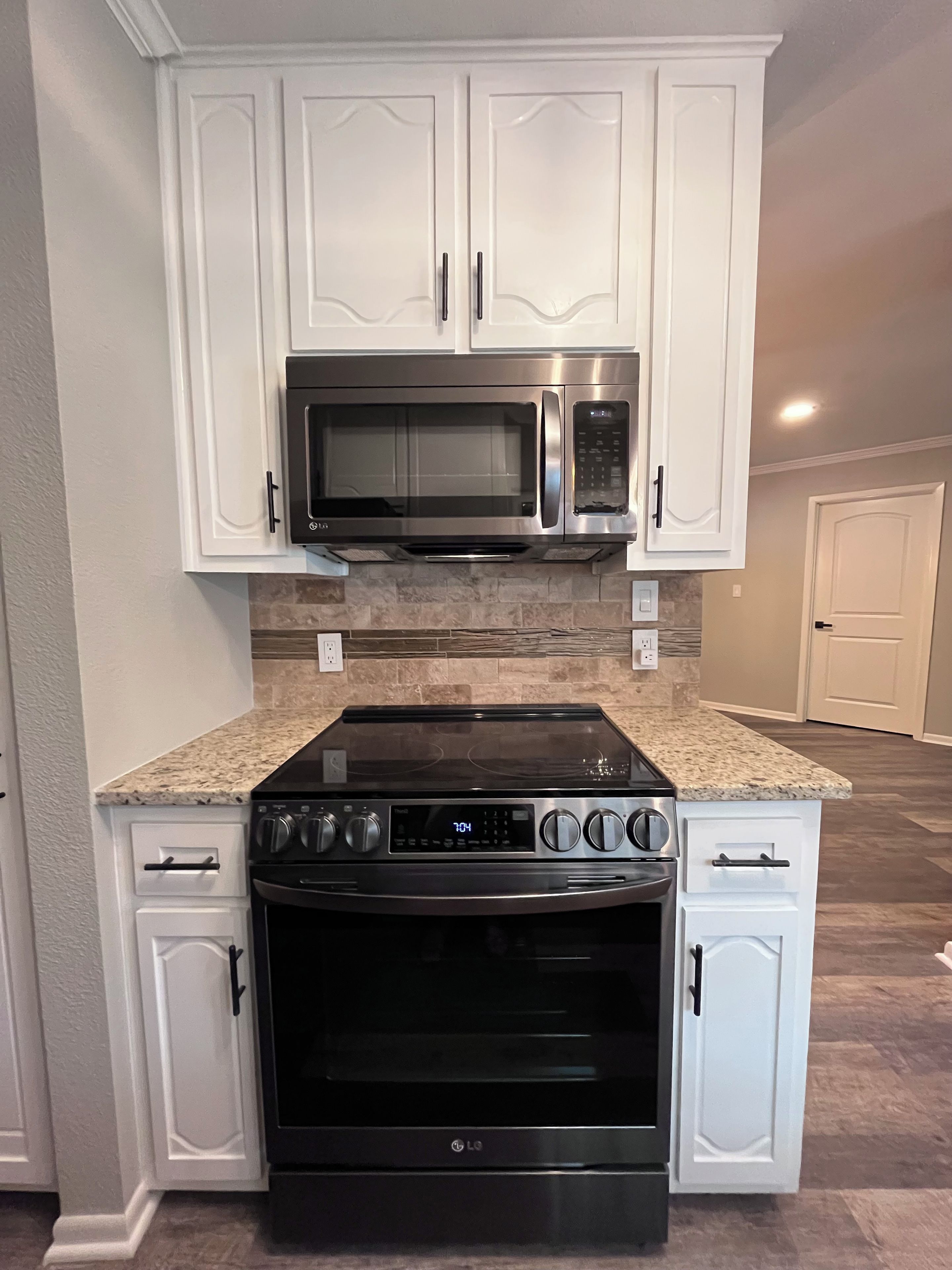Keittiössä on valkoiset kaapit, ruostumattomasta teräksestä valmistettu mikroaaltouuni ja musta LG-liesi.