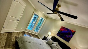 A bedroom with a bed, a ceiling fan, a nightstand, a lamp, and a window with blinds.