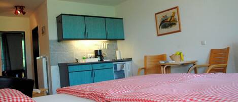 A hotel room with a bed, a desk, a chair, a small table, and a kitchenette.