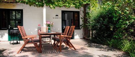 An outdoor patio with a wooden table and chairs, a grill, and a vase with flowers.