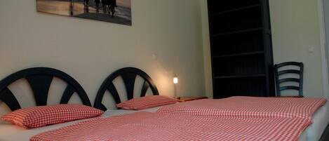 A bed with a checkered bedspread, a painting of people on horseback, a bookshelf, and a chair.