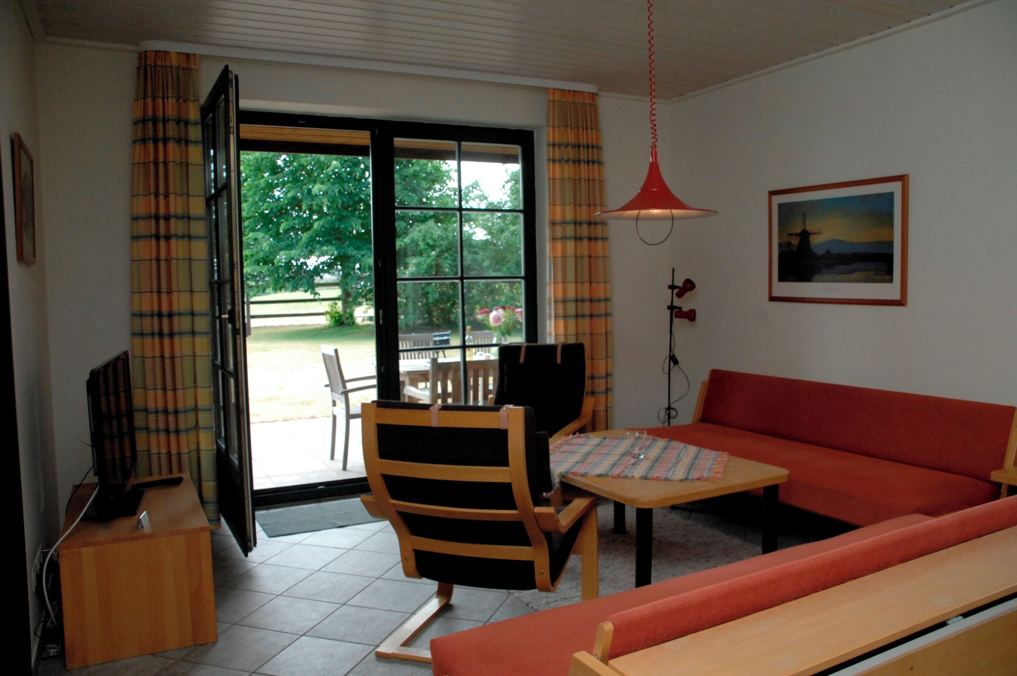 Una sala de estar con un sofá, una mesa, una silla, un televisor y una ventana con cortinas.