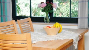 Une table en bois, sur laquelle se trouvent un saladier rempli de fruits et un vase de fleurs, près d’une fenêtre.