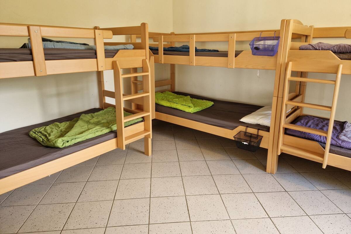 Quarto com beliche triplo, cada nível com estrutura e colchão de madeira.