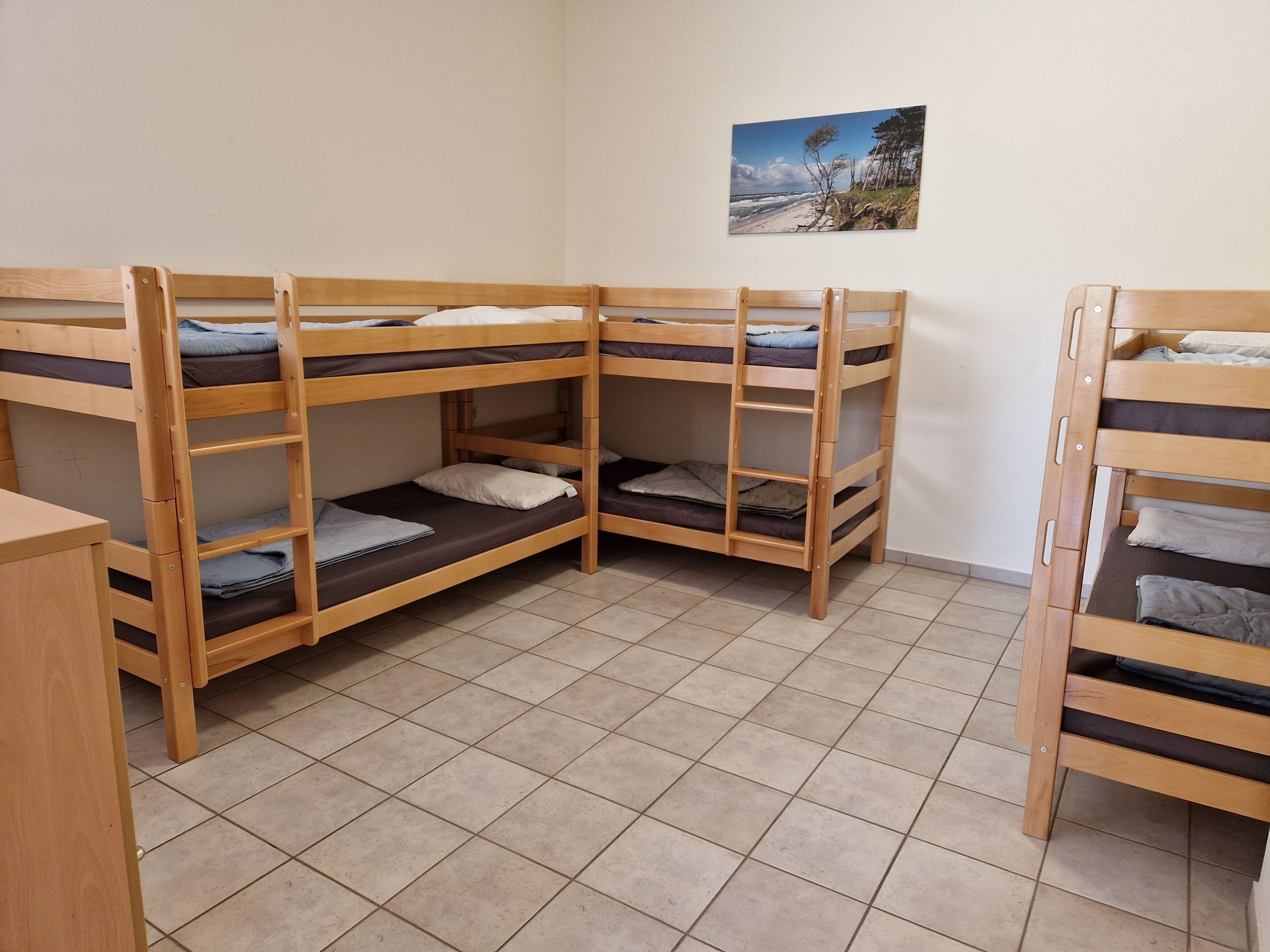 A dormitory room with bunk beds, tiled flooring, and a beach scene on the wall.