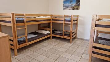 A dormitory room with bunk beds, tiled flooring, and a beach scene on the wall.