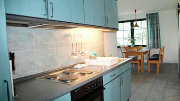 A kitchen with teal cabinets, a stove, and a dining area with a table and chairs.