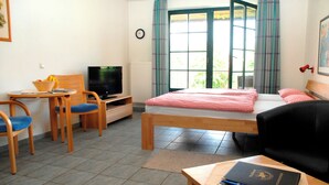 Une chambre d’hôtel comprenant un lit, un bureau avec une chaise, une télévision et une fenêtre avec des rideaux.