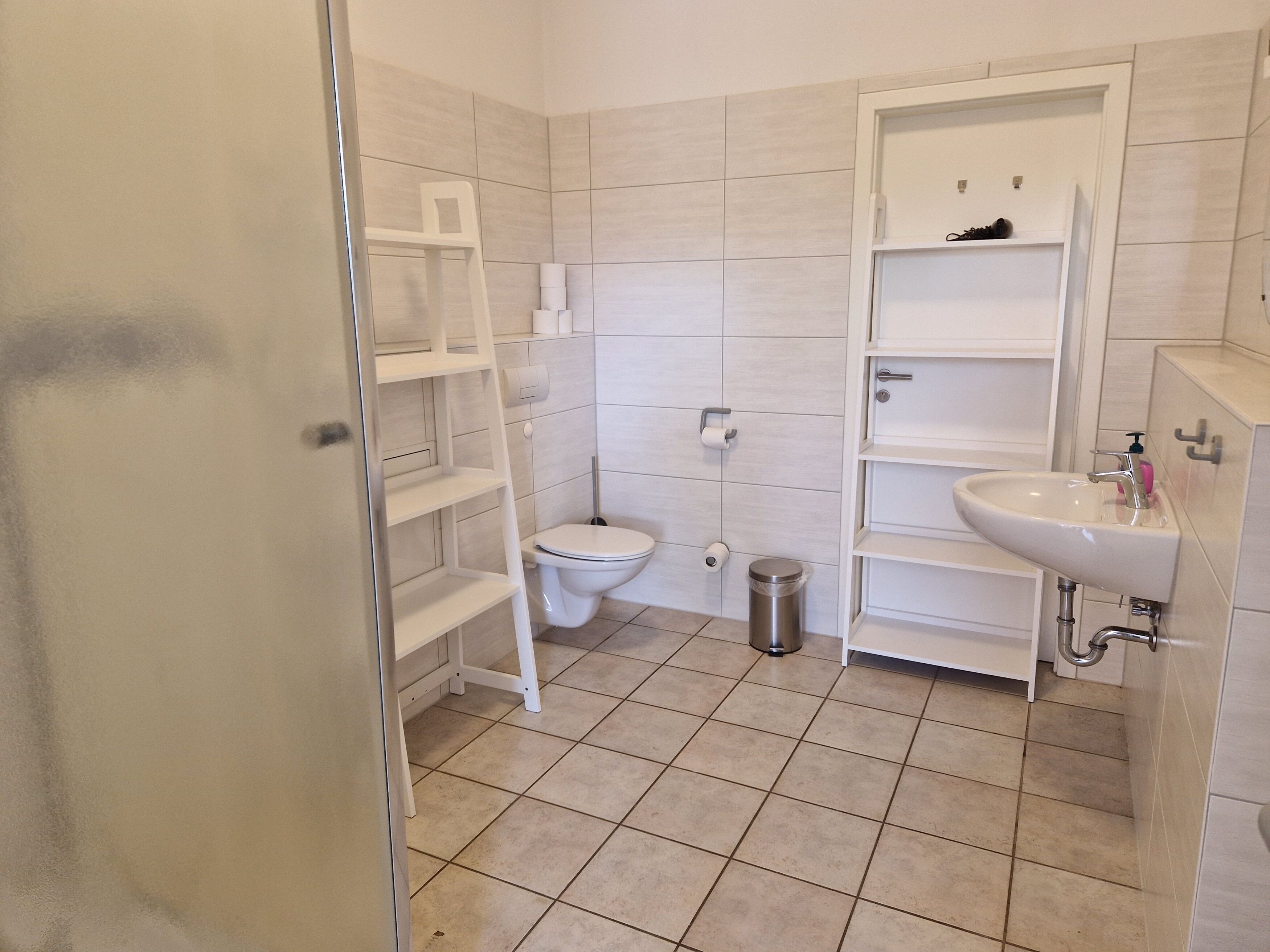 Ein Badezimmer mit Toilette, Waschbecken, Regalen und einem Mülleimer.