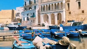 Un puerto con barcos amarrados, un edificio con arcos y un cielo azul despejado.