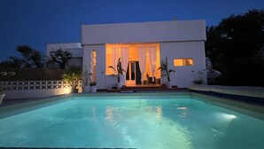 Una casa moderna con piscina, un porche cubierto y plantas en macetas.