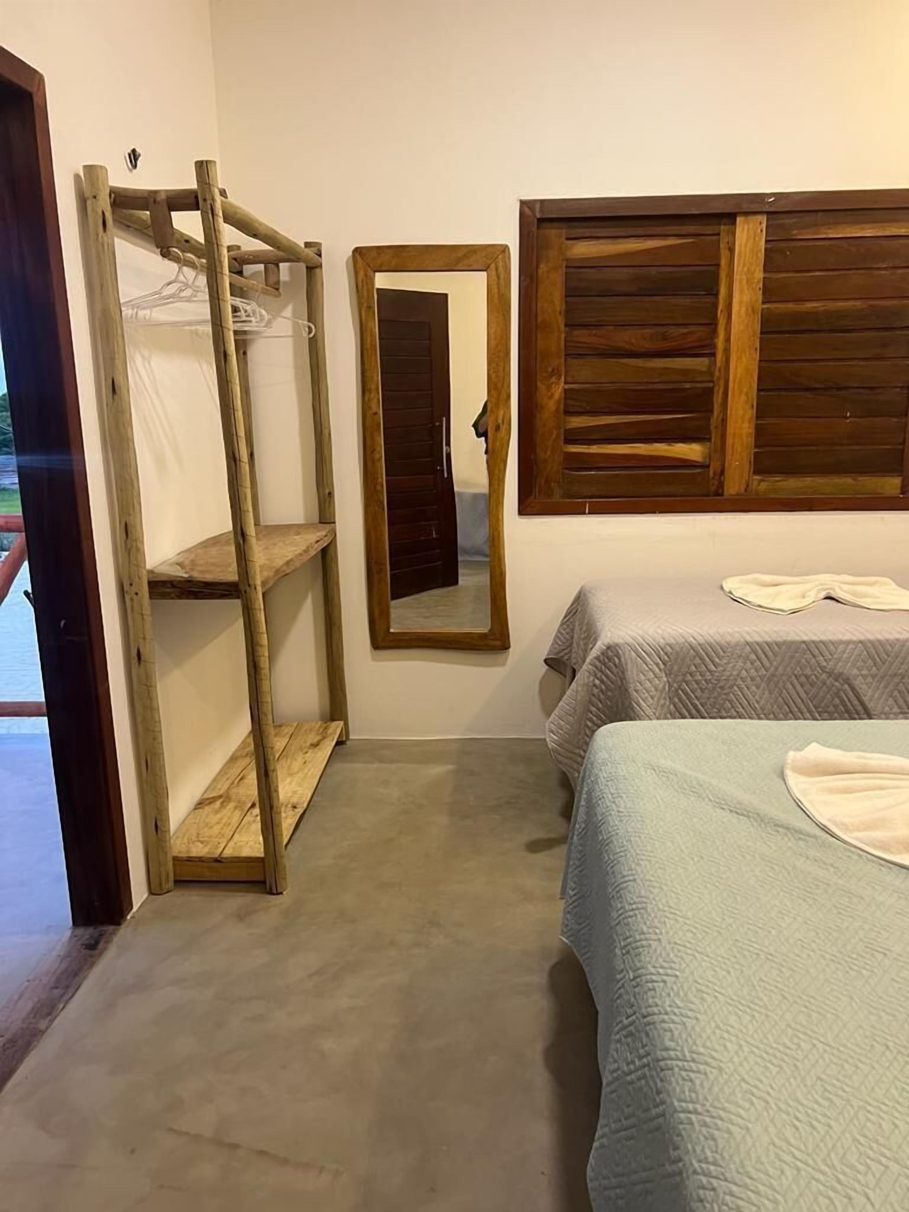 A bedroom with a wooden bunk bed, a bedside table, a mirror, and a window with wooden shutters.