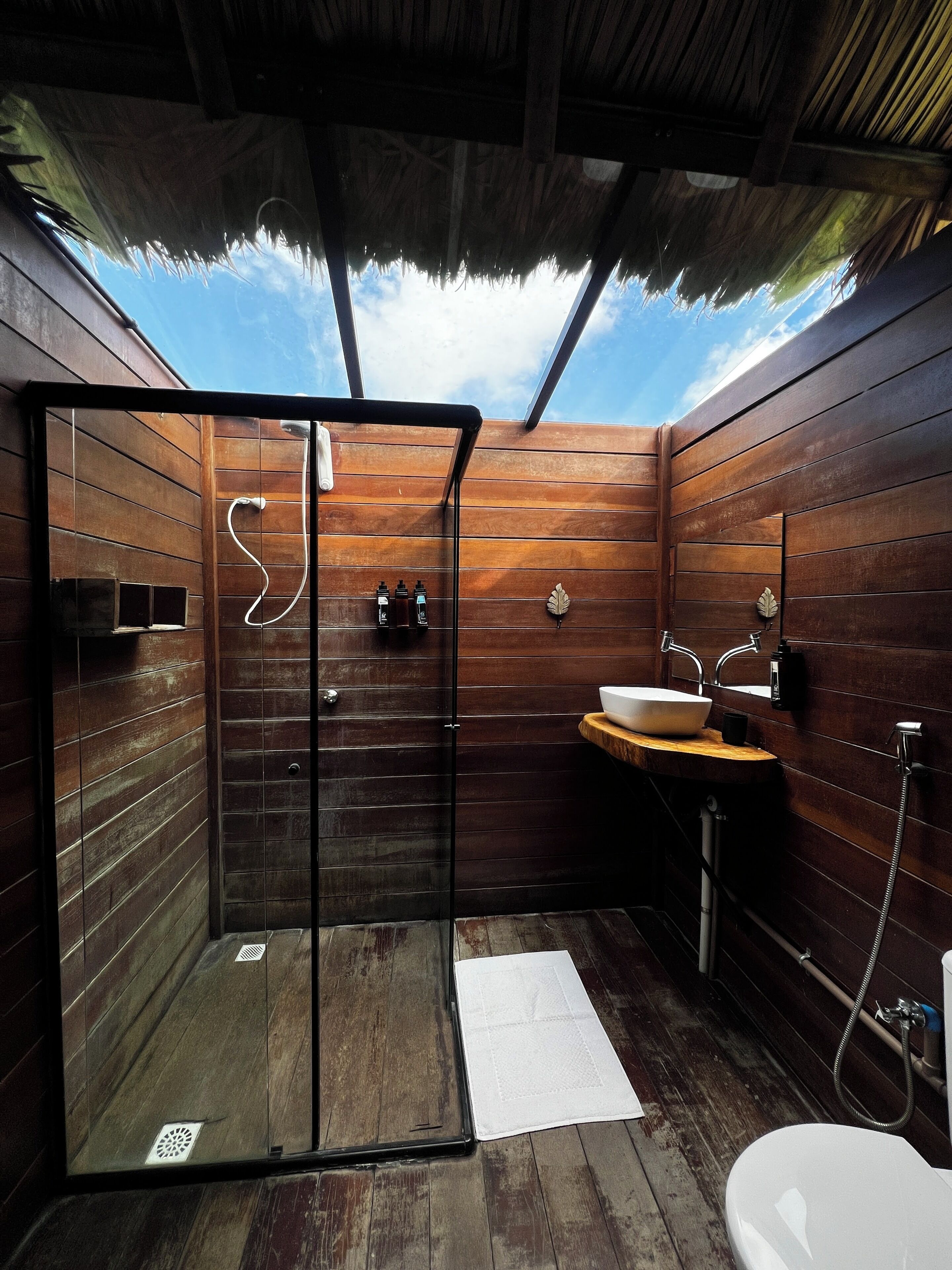 A modern bathroom with wooden walls, a glass shower enclosure, a wooden vanity, and a white sink.