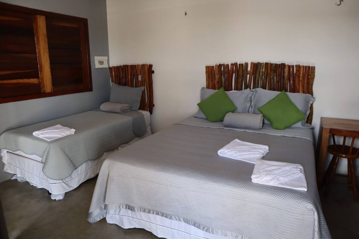 Dos camas individuales con ropa de cama gris y almohadas verdes, un cabecero de madera y una silla de madera.