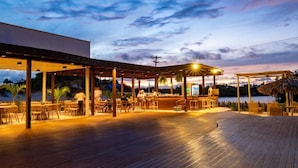 An outdoor bar area with wooden tables and chairs, a bar counter, and a view of the water. - Pacas Suítes (Santo Amaro do Maranhão)