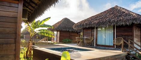 Una estructura de madera con techo de paja, piscina y terraza de madera.
