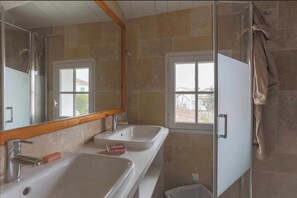 Two sinks with faucets and soap dishes, a large mirror, and a window offering a view of the outside.