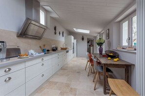 A modern kitchen with a built-in oven, a dining area with a wooden table and chairs, and a large window providing natural light. - Villa Luxueuse 4 Chambres Proche Plage / Luxurious Villa 4BR Near Beach (La Couarde-sur-Mer)