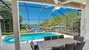 A covered outdoor area with a pool, wicker furniture, and a view of the surrounding landscape. - Private Canalfront Pool, Dock & Game Room | Dockside (Palm Coast)