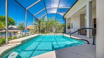 Piscina com estrutura de vidro, rodeada por um terraço com cadeiras e área de estar coberta.