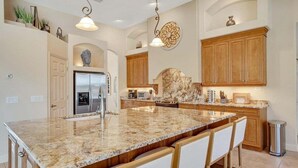 A spacious kitchen with a large granite island, wooden cabinets, and modern appliances. - Private Canalfront Pool, Dock & Game Room | Dockside (Palm Coast)