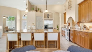 A modern kitchen with a central island, wooden cabinets, and pendant lighting. - Private Canalfront Pool, Dock & Game Room | Dockside (Palm Coast)