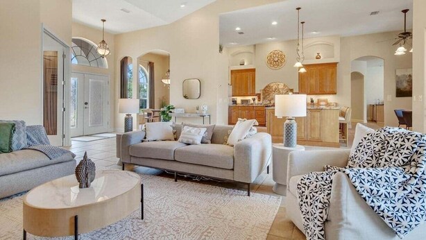 A spacious living room with a sofa, a coffee table, and a patterned throw. There is a kitchen area with wooden cabinets and a dining area visible in the background. - Private Canalfront Pool, Dock & Game Room | Dockside (Palm Coast)