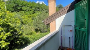 A balcony with a green door, a metal rack, and a brick chimney in the background.