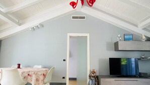 A dining area with a table and chairs, a red chandelier, a television, and a small doll.