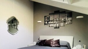 A modern bedroom with a skylight, a bed with grey bedding, a fluffy grey rug, and a wall-mounted mirror.